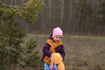 a little girl in a purple jacket plays with a toy in the woods and laughs