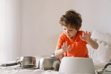 Cute young boy using wooden sticks to bang saucepans that are set up like a drumset.