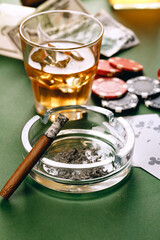 Glass of whiskey, cigar, playing cards and chips on green background