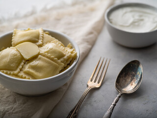 Ravioli or dumplings with sour cream or sauce on a light background