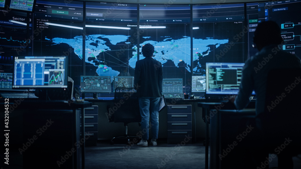 Poster Diverse Multiethnic IT Technical Support Manager with Curved Hair Stands next to Workplace in Monitoring Control Room Office with Big Digital Screens with Server Technical Blockchain Data.