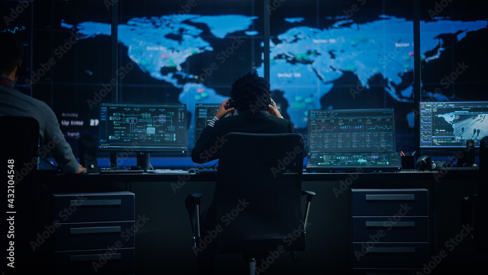 Poster Diverse Multiethnic IT Technical Support Manager with Curved Hair Puts on Headphones. Monitoring Control Room Office with Big Digital Screens with Server Technical Blockchain Data.