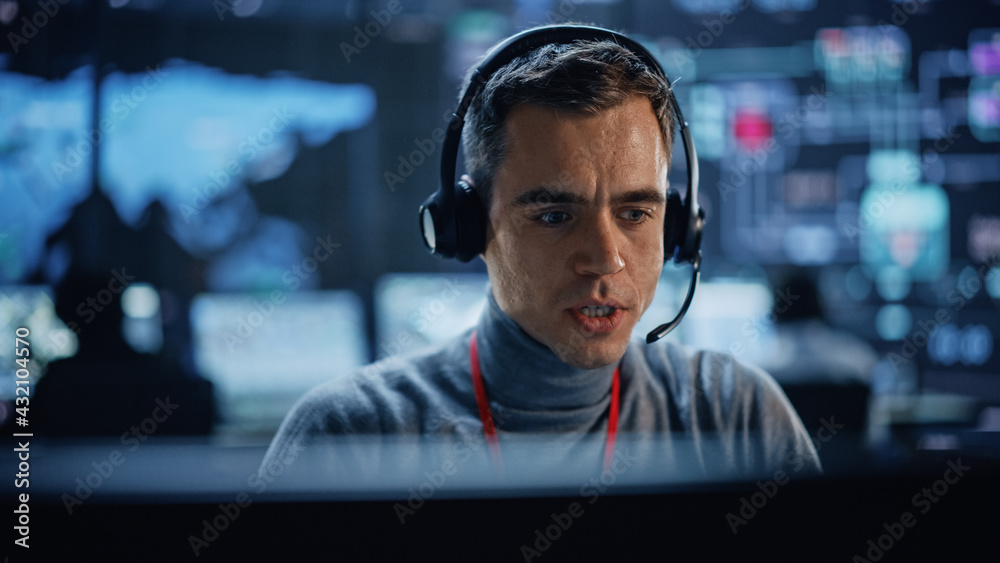 Poster Portrait of Professional IT Technical Support Specialist Working on Computer in Monitoring Control Room with Digital Screens. Employee Wears Headphones with Mic and Talking on a Call.