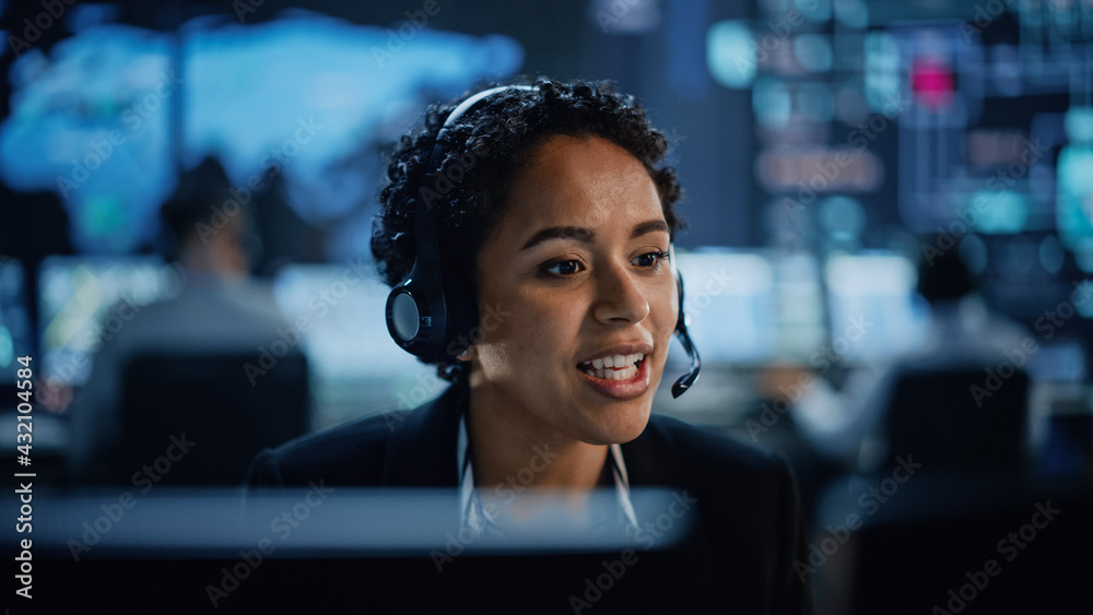 Poster Portrait of Professional IT Technical Support Female Specialist Working on Computer in Monitoring Control Room with Digital Screens. Employee Wears Headphones with Mic and Talking on a Call.
