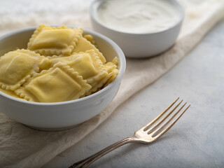 Ravioli or dumplings with sour cream or sauce on a light background
