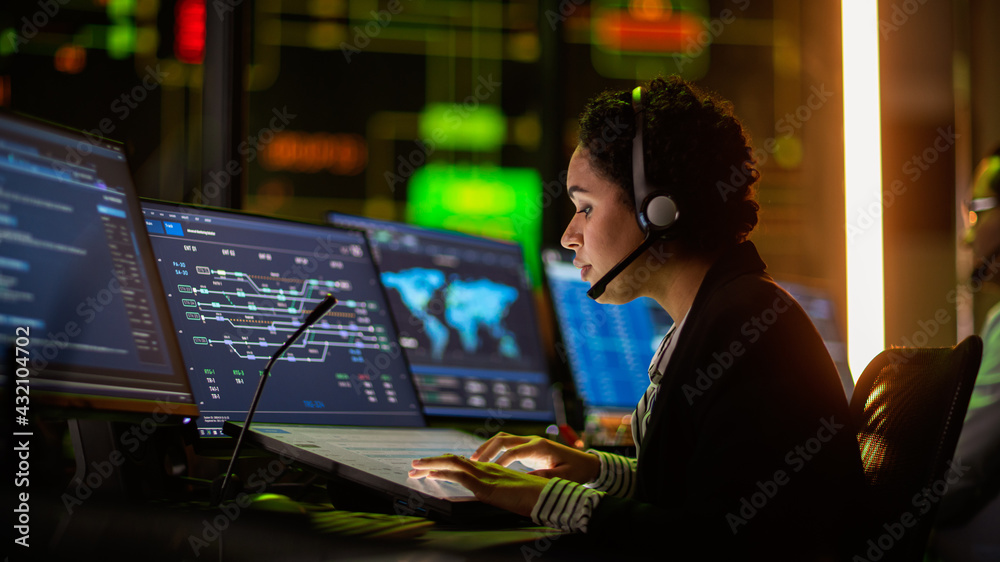 Poster Portrait of Professional IT Technical Support Specialist Working on Computer in Monitoring Control Room with Digital Screens. Employee Wears Headphones with Mic and Talking on a Call.