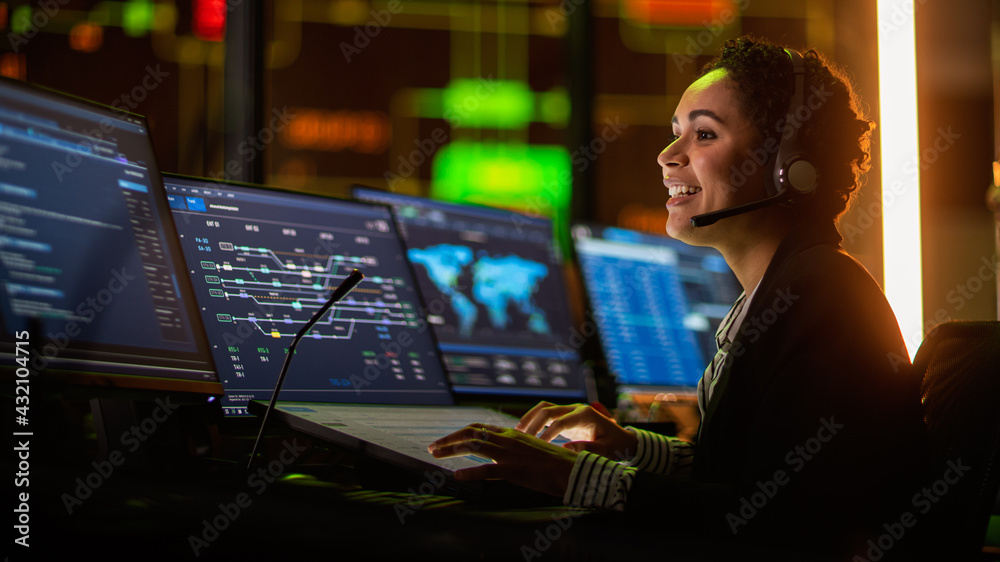 Poster Portrait of Professional IT Technical Support Specialist Working on Computer in Monitoring Control Room with Digital Screens. Employee Wears Headphones with Mic and Talking on a Call.