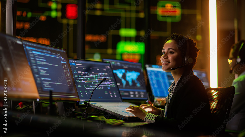 Poster Multiethnic Female IT Technical Support Specialist Talking with a Client in Headphones and Working on Desktop Computer in Monitoring Control Room with Big Digital Screens with Server Blockchain Data.