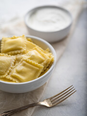 Ravioli or dumplings with sour cream or sauce on a light background