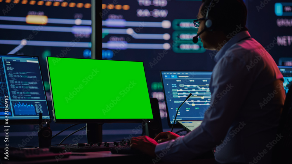 Poster Professional IT Technical Support Specialist and Software Developer Working on Computer with Green Screen Mock Up Display in Monitoring Control Room with Digital Screens. Employee Uses on Headphones.
