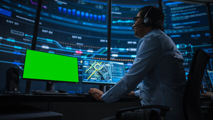 Professional IT Technical Support Specialist and Software Developer Working on Computer with Green Screen Mock Up Display in Monitoring Control Room with Digital Screens. Low Angle Shot.