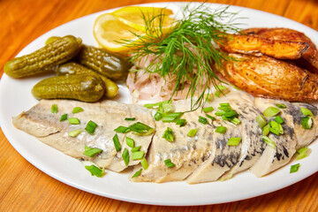 Pickled herring with pickles and herbs. Close-up, selective focus