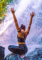 Beautiful young girl with black sport clothes standing in a waterfall 