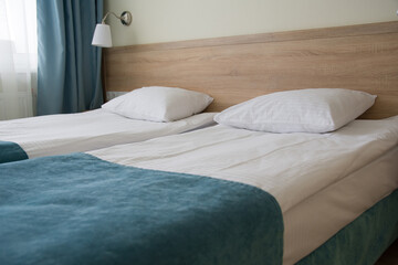 the interior of a small inexpensive hotel room for two with separate beds. The bed with fresh linen is covered with a turquoise blanket. the windows have turquoise curtains