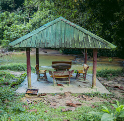 Fototapeta na wymiar Wooden and metal Gazebo with wooden Bench and tables next to a river in the green forest. Picnic concept. 