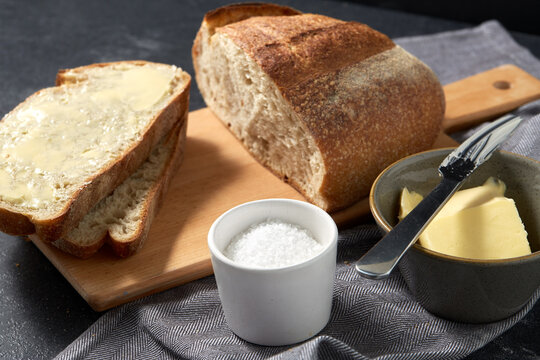 food, baking and cooking concept - close up of bread, butter in bowl, table knife and salt in cup on towel