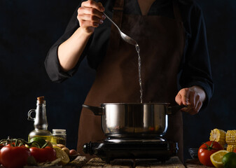 The chef cooks or prepares seafood soup in a saucepan on a background of ingredients. Cooking and recipes