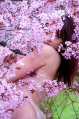 sensual, seductive, portrait of a sexy, young, brunette woman in pink dress in pink flower tree blossoms in spring awakening, sakura, copy space
