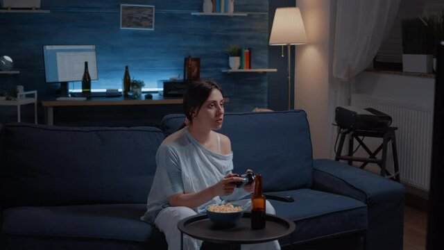 Focused determined woman playing video game late night concentrated trying to win online competition. Involved gamer sitting on couch, playing video games using joystick, wireless controller