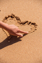 The girl draws a heart on the sand with her finger