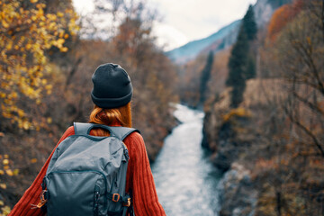 woman hiker with a backpack on her back near a mountain river in nature, back view