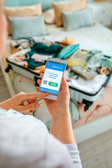 Unrecognizable woman preparing the suitcase and looking covid health passport on the mobile