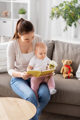family, motherhood and people concept - happy smiling mother reading book to little baby daughter...