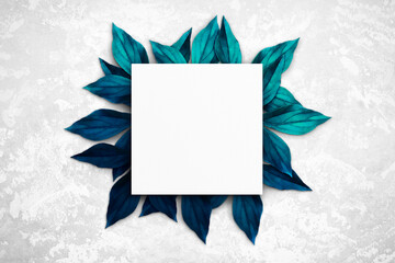Composition of empty white square watercolor sheet of paper, blue and turquoise leaves on a light gray concrete background. Advertising board, mockup on the wall. Flat lay, top view, copy space - obrazy, fototapety, plakaty