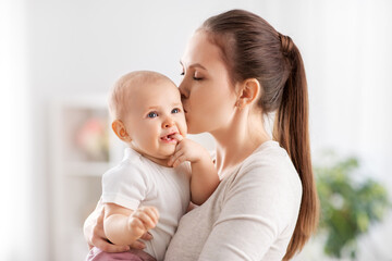 family, motherhood and people concept - happy mother kissing her little baby daughter at home
