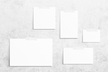 Composition of 5 empty white different sizes watercolor sheets of paper glued with scotch tape on light gray concrete background. Advertising board, mockup on the wall. Flat lay, top view, copy space