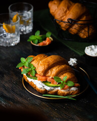 Croissant sandwich with salted salmon on black plate, served with fresh basil leaves, avocado and Philadelphia cheese. French breakfast. Healthy eating concept.