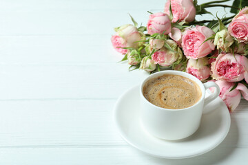 Beautiful roses and cup of coffee on white wooden background