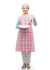 cooking, culinary and old people concept - smiling senior woman in kitchen apron with empty plate showing thumbs up over white background