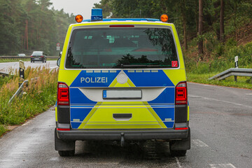 Rear view of a radio patrol car from the Brandenburg motorway in an emergency stopping bay. Police car in yellow and blue paintwork on a wet road. Blue light and police lettering on the tailgate