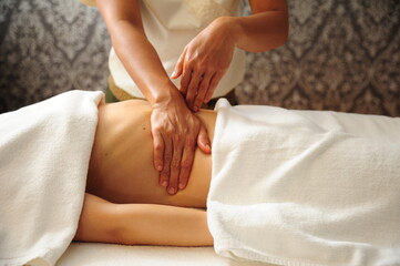Young beautiful woman at a session of a healing massage of the abdomen and internal organs, close-up. Masseuse kneads the muscles on the stomach of a young woman