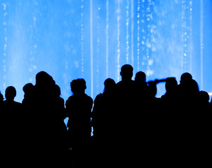 Silhouettes of people at the blue fountain at night.