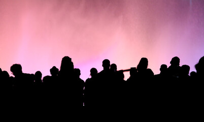 Fototapeta na wymiar Silhouettes of people at a colored fountain at night.