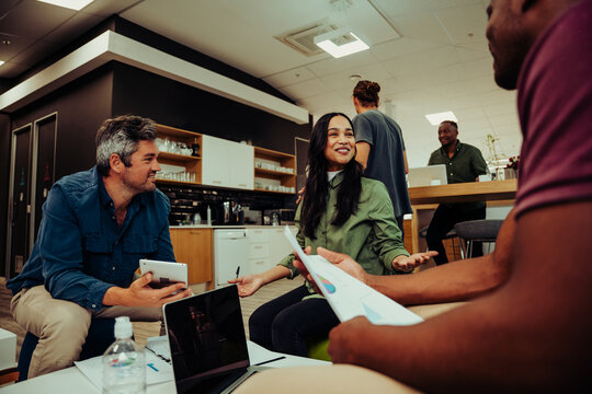 Diverse group of people having meeting in office lounge discussing new project working on laptops and through paper work 