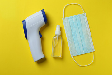 Medical tools and thermometer gun on yellow background