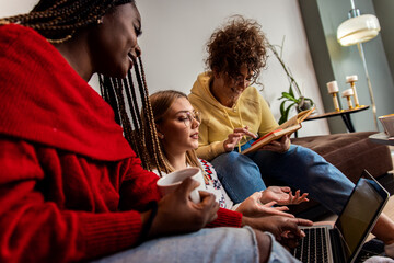 Multiethnic female students learning at home using laptop and books for research.