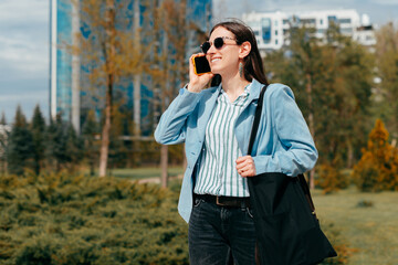 A cheerful young business woman is talking with someone on her phone in park being positive