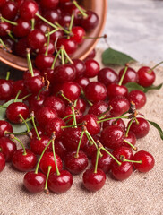 Bowl with red cherry on sackcloth background, top view