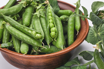 Pods of green peas with leaves in bowl