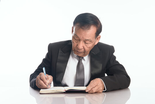 Close up older asian business man putting signature on legal documents. Senior man  freelancer writing details on book on desk in living room.