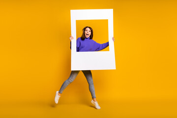 Photo of charming sweet young woman wear purple sweater jumping holding white photo frame isolated orange color background