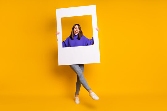 Photo of shiny pretty young lady dressed violet pullover walking holding photo frame isolated orange color background