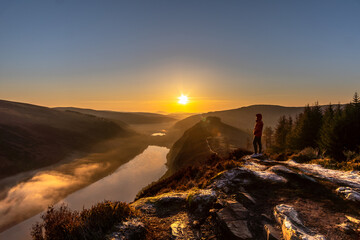 A Man in orange jacket standing on the Spink Viewing Spot admiring the sunrise in Wicklow Ireland