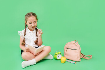 Cute schoolgirl in uniform sitting on green background and reeding book, copy space