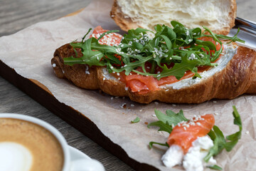 Cappuccino and bun breakfast at the cafe. American morning. Croissant with trout and arugula