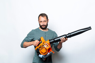 Fototapeta na wymiar I'm ready to go and start up my leaf blower. Studio portrait of Serious man holds in Hands blower machine. Handsome Caucasian Worker looking at camera. People, lifestyle and technology concept